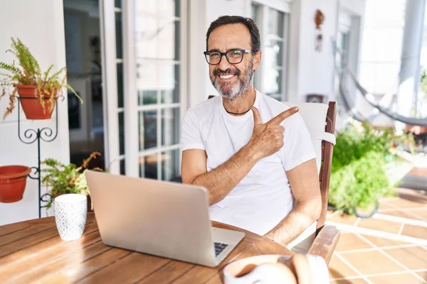 家でコンピュータのラップトップを使用している中年の男陽気な笑顔で顔を指差す手と指で幸せと自然な表情で側面まで — ストック写真