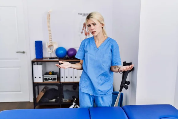 痛みの回復クリニックで働いている若い理学療法士の女性は無知で開かれた腕と混同されています 概念はありません — ストック写真