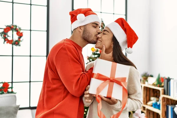 Young Hispanic Couple Kissing Hugging Holding Christmas Gift Home — Stock Photo, Image