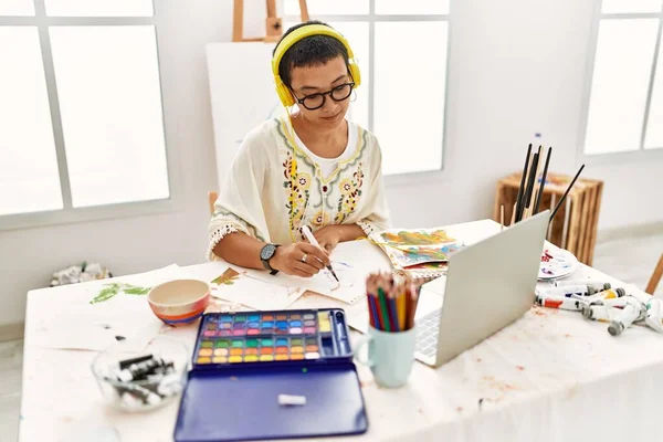 年轻的惊慌失措的女人在艺术工作室里一边听音乐一边用笔记本电脑在笔记本上画画 — 图库照片