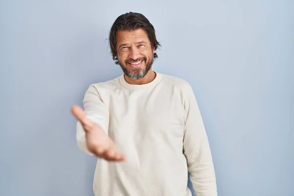 青い背景にカジュアルなセーターを着たハンサムな中年の男性が挨拶や歓迎として握手を提供する優しい笑顔 成功したビジネス — ストック写真