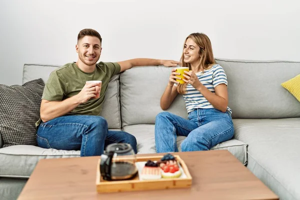 Genç İspanyol çift mutlu bir şekilde gülümsüyor. Evdeki kanepede oturup kahvaltı yapıyorlar..