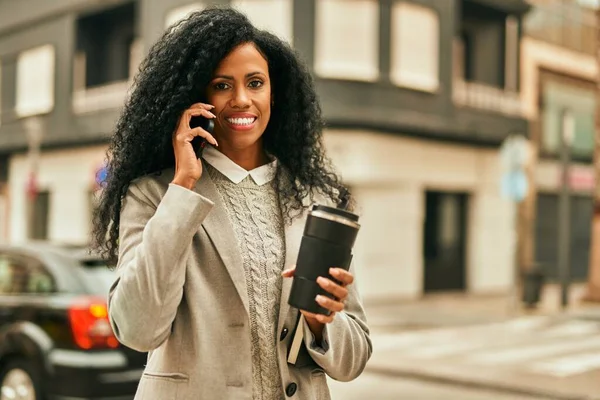Orta yaşlı Afro-Amerikan iş kadını akıllı telefondan konuşuyor ve şehirde kahve içiyor..