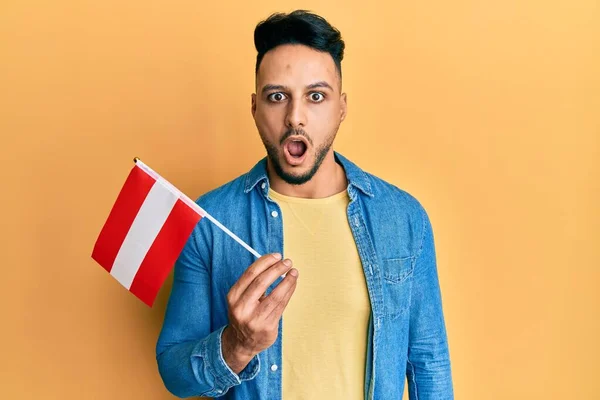 Młody Arabski Mężczyzna Trzymając Austriacką Flagę Przestraszony Zdumiony Otwartymi Ustami — Zdjęcie stockowe