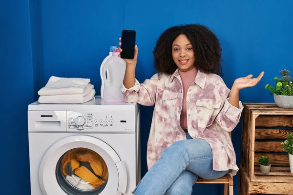 年轻的非洲裔美国女人用智能手机洗衣服 带着快乐的笑容和高傲的表情庆祝自己的成就 — 图库照片