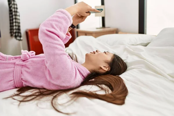 年轻的中国姑娘用智能手机躺在卧室的床上 — 图库照片