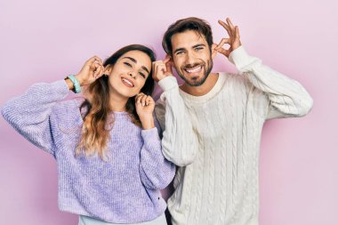Genç İspanyol çift, günlük kıyafetler giyip gülümsüyor kulaklarını parmaklarıyla çekiyor, komik bir jest. deneme sorunu 