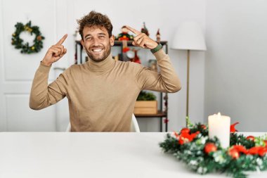 Masaya sakallı yakışıklı bir adam oturmuş Noel süslemeleriyle gülümsüyor iki eliyle başını işaret ediyor, harika bir fikir ya da düşünce, iyi bir hafıza. 