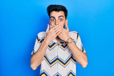 Gündelik kıyafetler giyen genç İspanyol adam yanlışlıkla elleri ile ağzını kapatırken şok oldu. gizli kavram. 