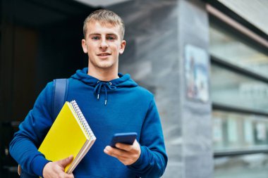 Üniversitede akıllı telefon kullanan genç sarışın bir öğrenci..