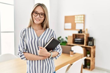 Ofiste kitap tutan genç Çinli kadın gülümsüyor.
