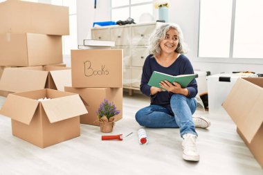 Orta yaşlı, kır saçlı, gülümseyen, yeni evinde mutlu bir kitap okuyan kadın..