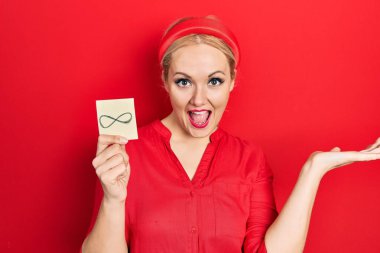 Genç sarışın kadın sonsuz bir sembol tutuyor zaferi mutlu bir gülümsemeyle ve kazanan yüz ifadesiyle kutluyoruz. 