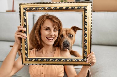 Beyaz kadın elinde boş bir çerçeve tutuyordu. Evde köpekle oturuyordu.