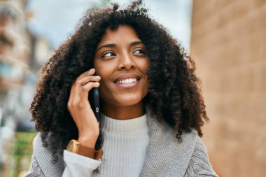 Genç Afrikalı Amerikalı kadın gülümsüyor. Şehirdeki akıllı telefondan mutlu bir şekilde konuşuyor..