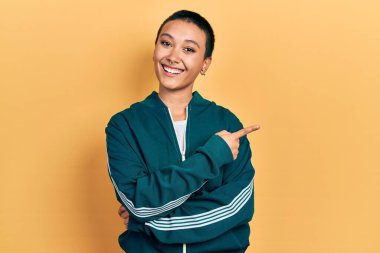 Güzel, kısa saçlı, spor ceketli, yüzünde kocaman bir gülümseme olan, eli ve parmağı kameraya bakan İspanyol bir kadın.. 