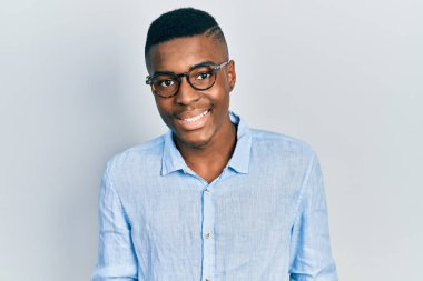 Yüzünde mutlu ve havalı bir gülümseme olan gündelik kıyafetler ve gözlük takan genç Afro-Amerikan bir adam. şanslı kişi. 