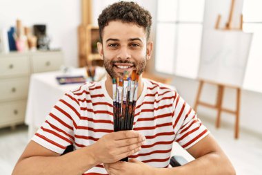 Genç Arap, resim stüdyosunda tekerlekli sandalyede fırça tutan engelli bir sanatçı..
