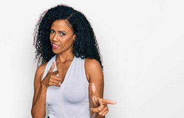 Orta yaşlı Afro-Amerikalı kadın kolsuz tişörtlü, gündelik giyinmiş mutlu ve komik yüzlü parmakları kameraya doğrultuyor. iyi enerji ve titreşimler. 