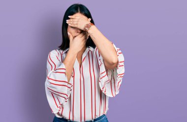 Gündelik kıyafetler giyen genç İspanyol kız gözlerini ve ağzını elleriyle kapatıyor, şaşırmış ve şok olmuş. duygu gizleme 