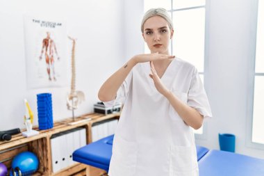 Ağrı kesici kliniğinde çalışan genç beyaz bir kadın. Elleriyle jest yapıyor. Hayal kırıklığına uğramış ve ciddi bir yüz ifadesi var. 