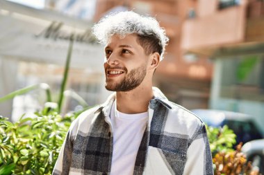 Genç İspanyol adam gülümseyerek şehirde mutlu mesut dikiliyor..