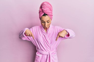 Duş havlusu şapkası ve bornoz takan genç sarışın kadın. İlan veren parmaklarıyla işaret ediyor. Şaşırmış yüz ve ağzı açık. 