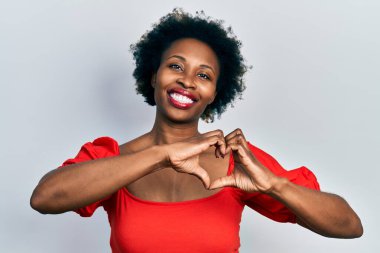 Genç Afro-Amerikan kadın, günlük kıyafetler giyip, aşıkken gülümsüyor, elleriyle kalp sembolü yapıyor. romantik kavram. 