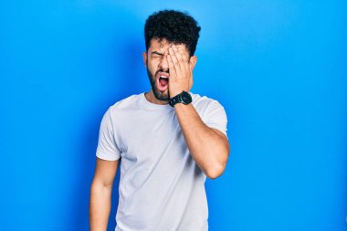 Sakallı, günlük beyaz tişörtlü, yorgun, yarı yüz, göz ve ağız kaplayan genç bir Arap. Yüzüm acıyor.. 