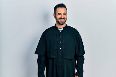 Sakallı yakışıklı, Katolik rahip cübbesi giyen yakışıklı bir adam kameraya seksi bir ifadeyle bakıyor, neşeli ve mutlu bir yüzle.. 