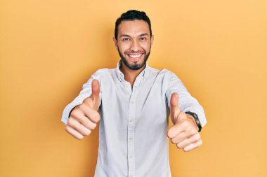 Sakallı, iş gömleği giyen, elinde olumlu bir jest yapmayı onaylayan, gülümseyen ve başarı için mutlu bir İspanyol. kazanan jest. 