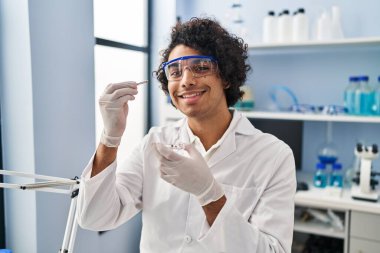 Laboratuvarda elinde cımbızla bilim adamı üniforması giyen genç bir İspanyol.