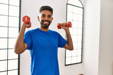 Yakışıklı İspanyol adam spor salonunda egzersiz yapıyor. Elinde dambıllar var.