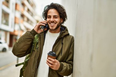 Yakışıklı İspanyol adam telefonda konuşuyor. Duvara yaslanıyor.