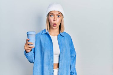 Güzel sarışın kadın bir fincan kahve içiyor korkmuş ve şaşırmış bir şekilde ağzı açık, inançsız bir yüz. 