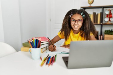 Afro-Amerikalı kız gülümseyerek evde ödevini yapıyor.