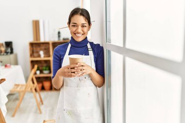 Genç Latin kadın gülümsüyor. Sanat stüdyosunda kahve içiyor.