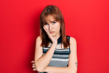 Kızıl saçlı genç kadın rahat bir tişört giyip kollarını kavuşturup depresyondan sıkılmış ve yorgun görünüyor.. 