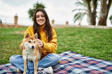 Güzel genç bir kadın parkta mutlu Shiba Inu köpeğine sarılıyor.