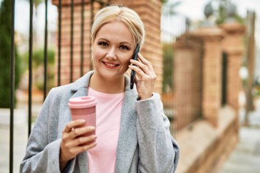 Sarışın iş kadını akıllı telefondan konuşuyor. Şehirde kahve içiyor..