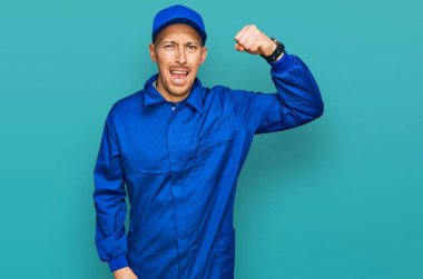 Kel ve sakallı bir adam, inşaatçı üniforması giyiyor. Kızgın ve kızgın. Öfkeyle bağırırken yumruğunu kaldırıyor. öfke ve agresif konsept. 