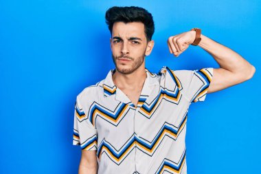 Gündelik kıyafetler giyen genç İspanyol adam güçlü kol kası gösteren, kendinden emin ve gururlu biri. 