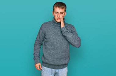 Sıradan kıyafetler giyen genç bir adam diş ağrısı ya da diş hastalığından dolayı acı dolu bir ifadeyle ağıza dokunuyor. dişçi 