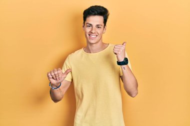 Sarı günlük tişörtler giyen genç İspanyol adam arka tarafı işaret ediyor. El ve baş parmakları havada, kendine güvenen. 