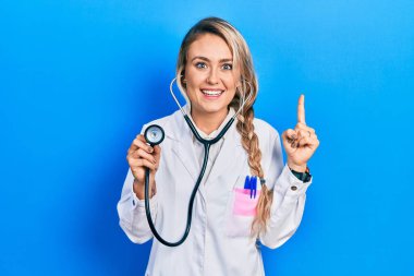 Güzel sarışın doktor kadın steteskop tutuyor. Şaşırmış, şaşırmış, parmaklarıyla işaret ediyor ve kollarını kaldırıyor.. 