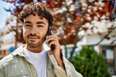 Yakışıklı, sakallı, güneşli bir günde dışarıda mutlu bir şekilde gülümseyen telefonda konuşan İspanyol bir adam.