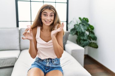 Genç sarışın kadın, elinde regl kupası tutarak zaferi kutluyor. Mutlu bir gülümseme ve ellerini kaldırarak kazanan bir ifadeyle. 