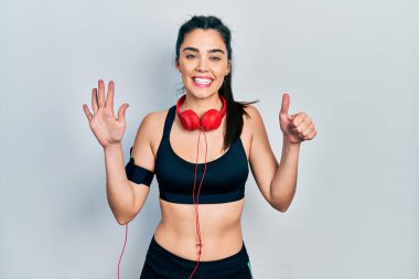 Spor kıyafetleri giyen ve kulaklık takan genç İspanyol kız altı numarayı gösterip işaret ederken kendinden emin ve mutlu bir şekilde gülümsüyor.. 