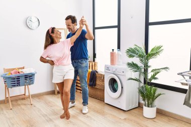 Çamaşırhanede dans eden ve çamaşır yıkayan orta yaşlı bir erkek ve kadın.