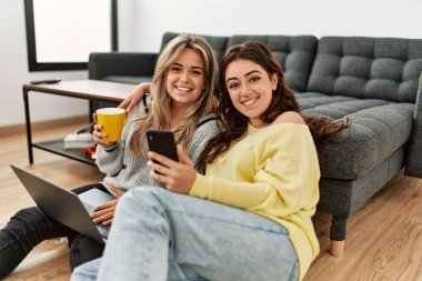 Young couple using laptop and smartphone drinking coffee at home. clipart
